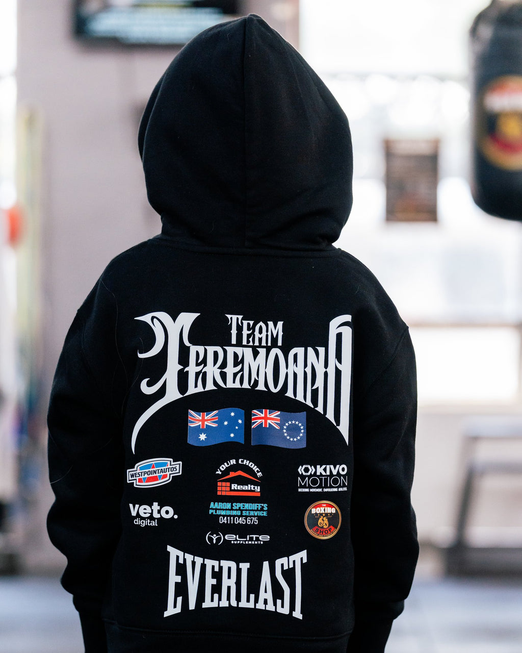 Back of the kids black Team Teremoana Hoodie with the hood up, showing the full back print