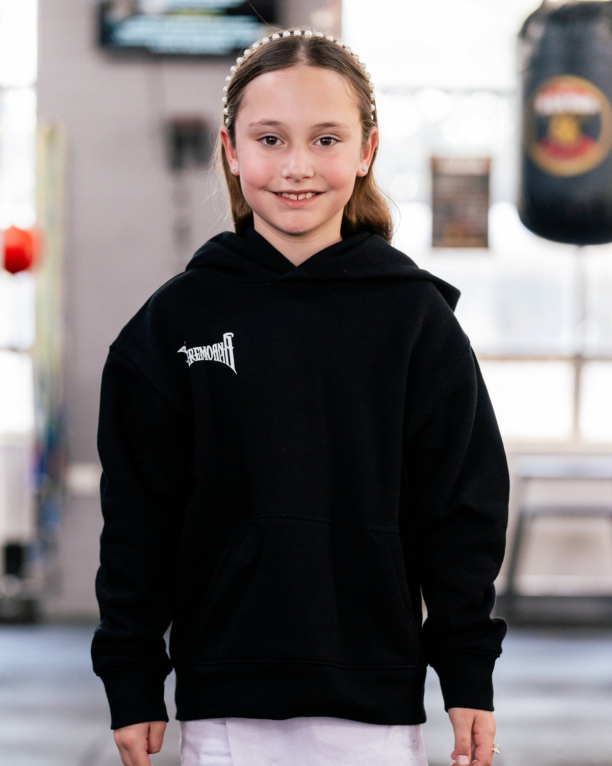 Girl wearing the kids black Team Teremoana Hoodie, front view
