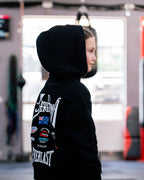 Side view of a girl in the kids black Team Teremoana Hoodie with the hood up, showing the back print