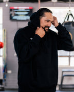 Teremoana pulling up the hood of the black Team Teremoana Hoodie in the gym