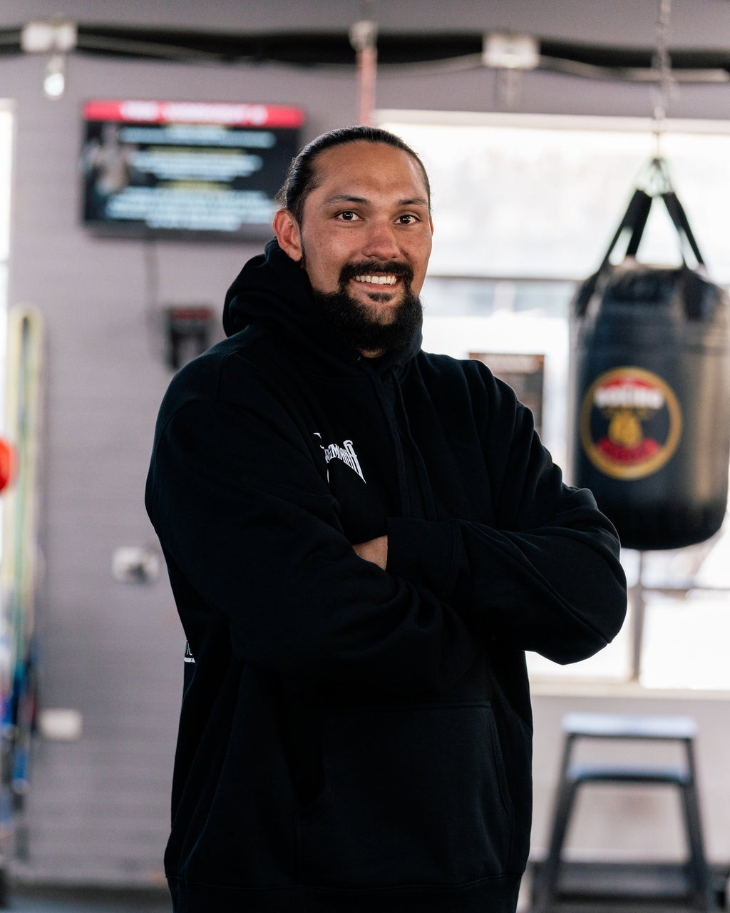 Teremoana in the black Team Teremoana Hoodie, arms crossed, showing the relaxed fit