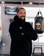 Teremoana in the black Team Teremoana Hoodie, arms crossed, showing the relaxed fit