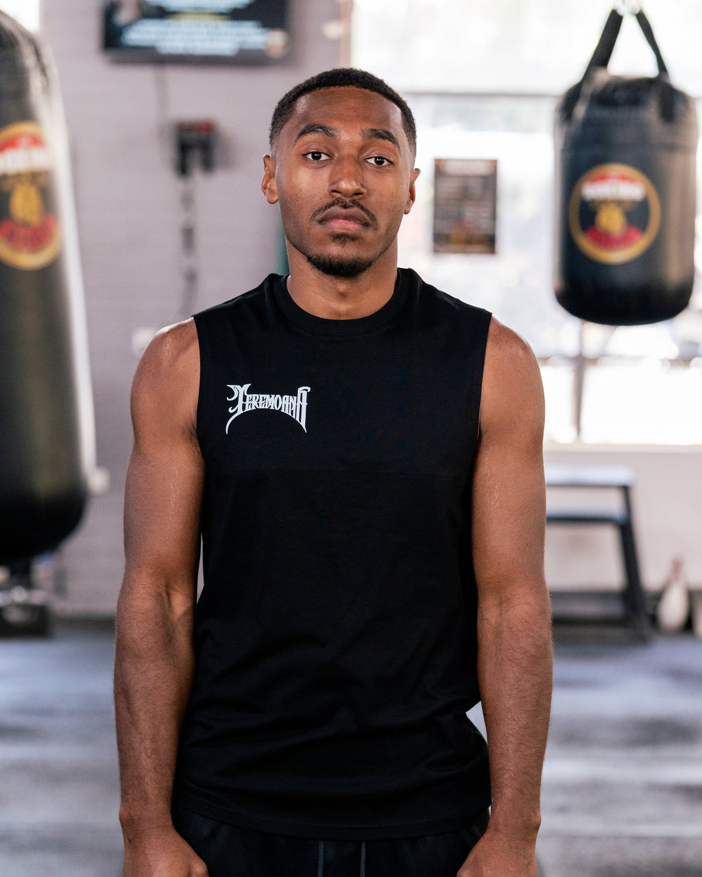 Teremoana wearing the black Team Teremoana Muscle Tank, front view by the punching bags