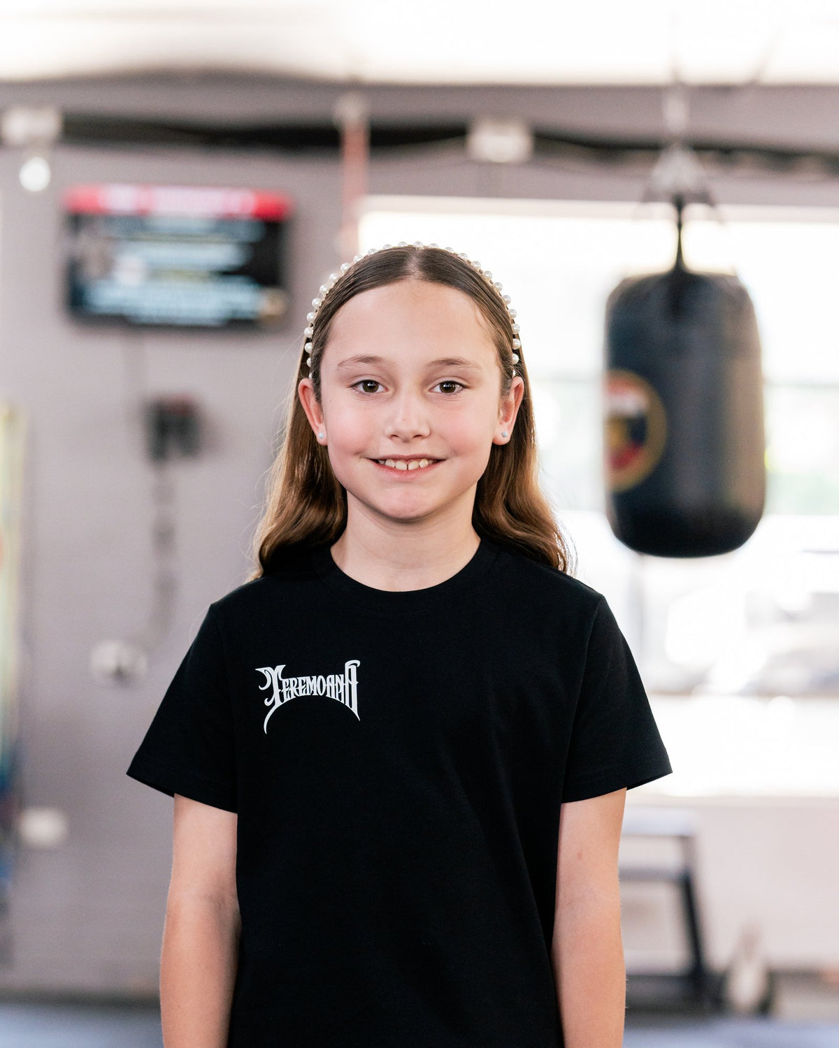 Child wearing the kids black Team Teremoana Tee in the gym, front view