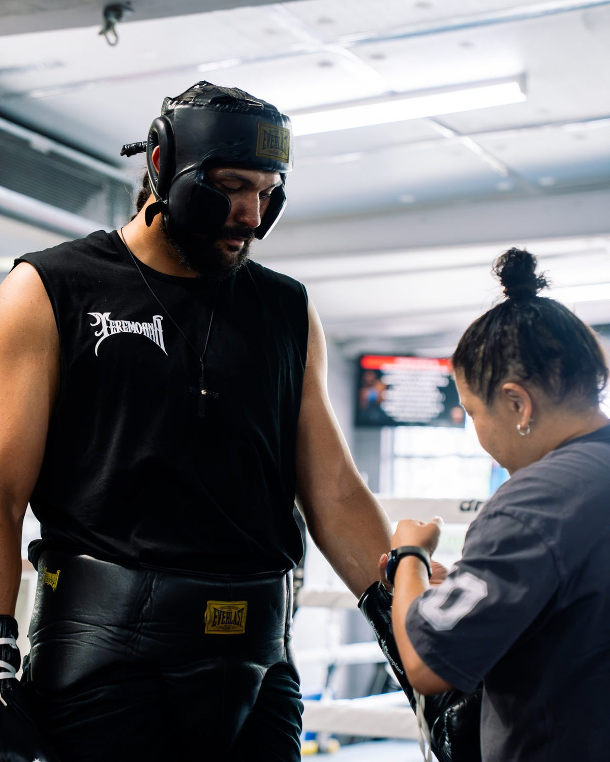 Teremoana in headgear and a Team Teremoana tank having his hands wrapped by his team in camp